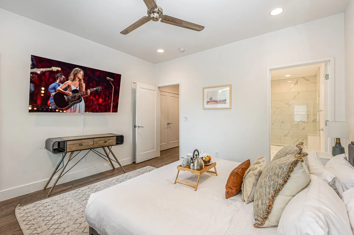 A cozy interior bedroom scene with a comfortable bed, decorative pillows, a side table, and a television featuring a performance. The ambiance is inviting, perfect for relaxation after a day out in the city.