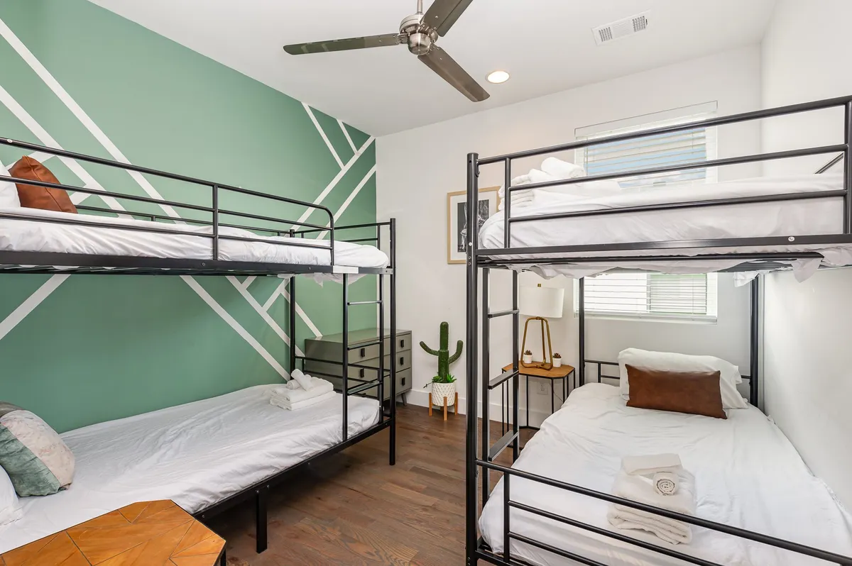 A playful bunk room featuring multiple bunk beds, a lively green accent wall, a decorative side table, and a potted plant. The layout is inviting for both children and adults, fostering a cozy and social environment.