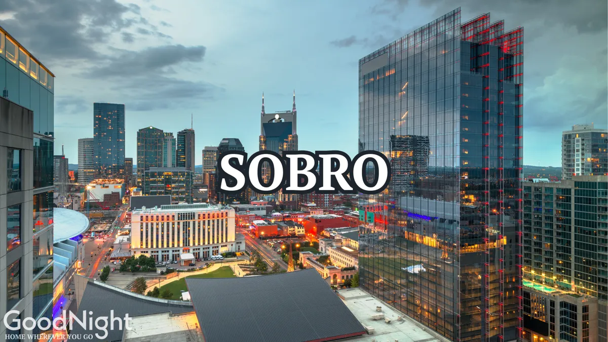 A sweeping view of Nashville’s city skyline at dusk, with illuminated buildings and the prominent 'SOBRO' sign, capturing the energetic ambiance of the area.