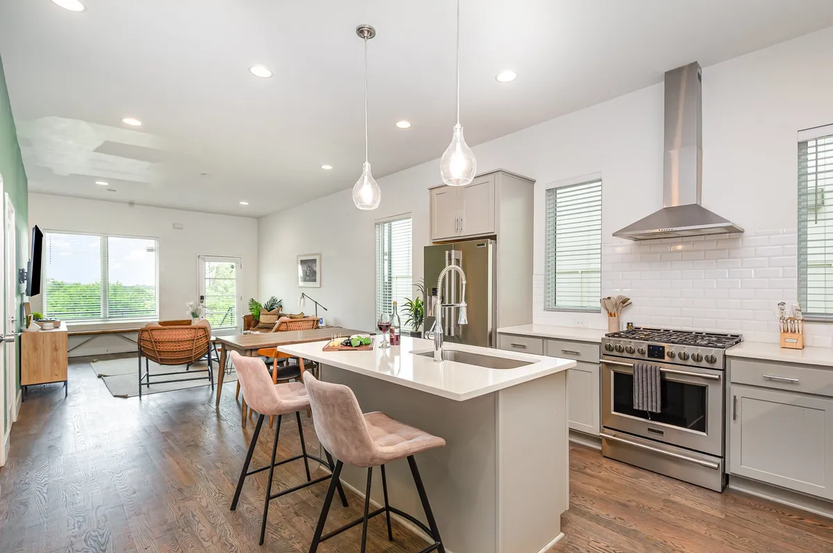 A modern kitchen and dining area with a kitchen island, stainless steel appliances, large windows, and an adjoining dining space. The open layout encourages conversation and togetherness, with ample seating for group meals or casual gatherings.