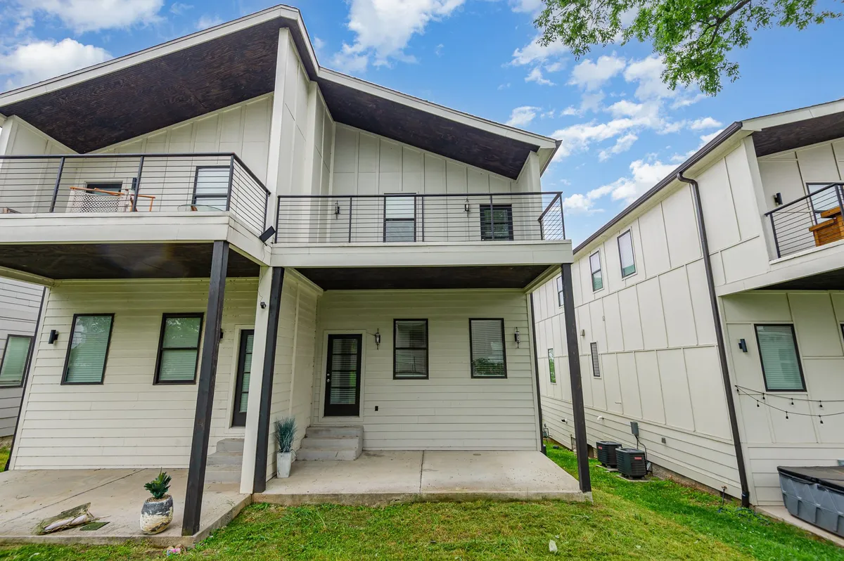 A welcoming exterior shot featuring a modern single-family home with a front porch, a visible balcony above, and a green lawn. The architecture is contemporary, and the balcony provides a sense of private outdoor space, while the visible driveway and garage hint at ample parking options.