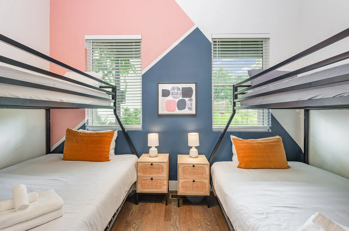 A vibrant bunk room with colorful wall designs, a set of sturdy bunk beds, cheerful bedding, nightstands with reading lamps, and playful artwork. The room exudes a youthful, communal energy ideal for sleepovers and group stays.